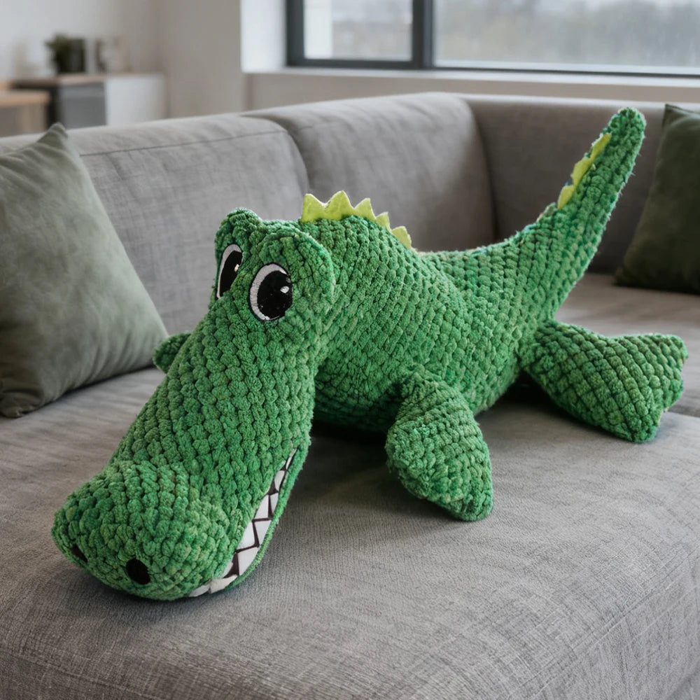 Peluche crocodile AventureCanine verte en tissu doux avec couineur pour chien sur un canapé gris